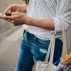 woman walks down the street and texts with a bag of groceries on her arm